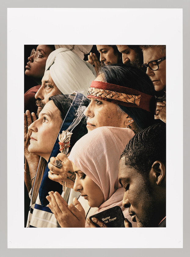 A diverse group of people from different faiths stand closely together in prayer.