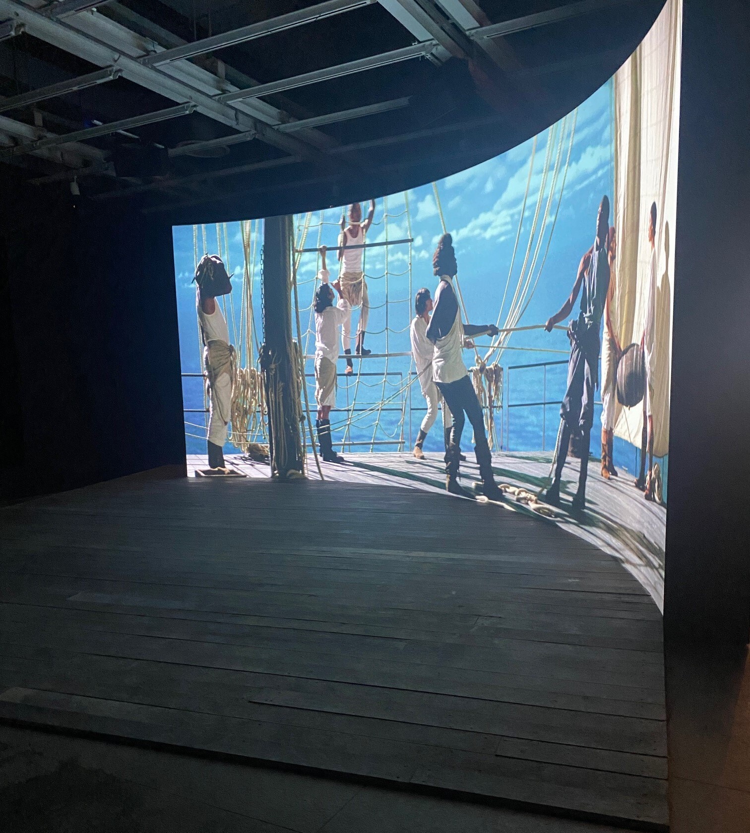 Sailors on a ship work together hoisting sails and handling ropes on deck.