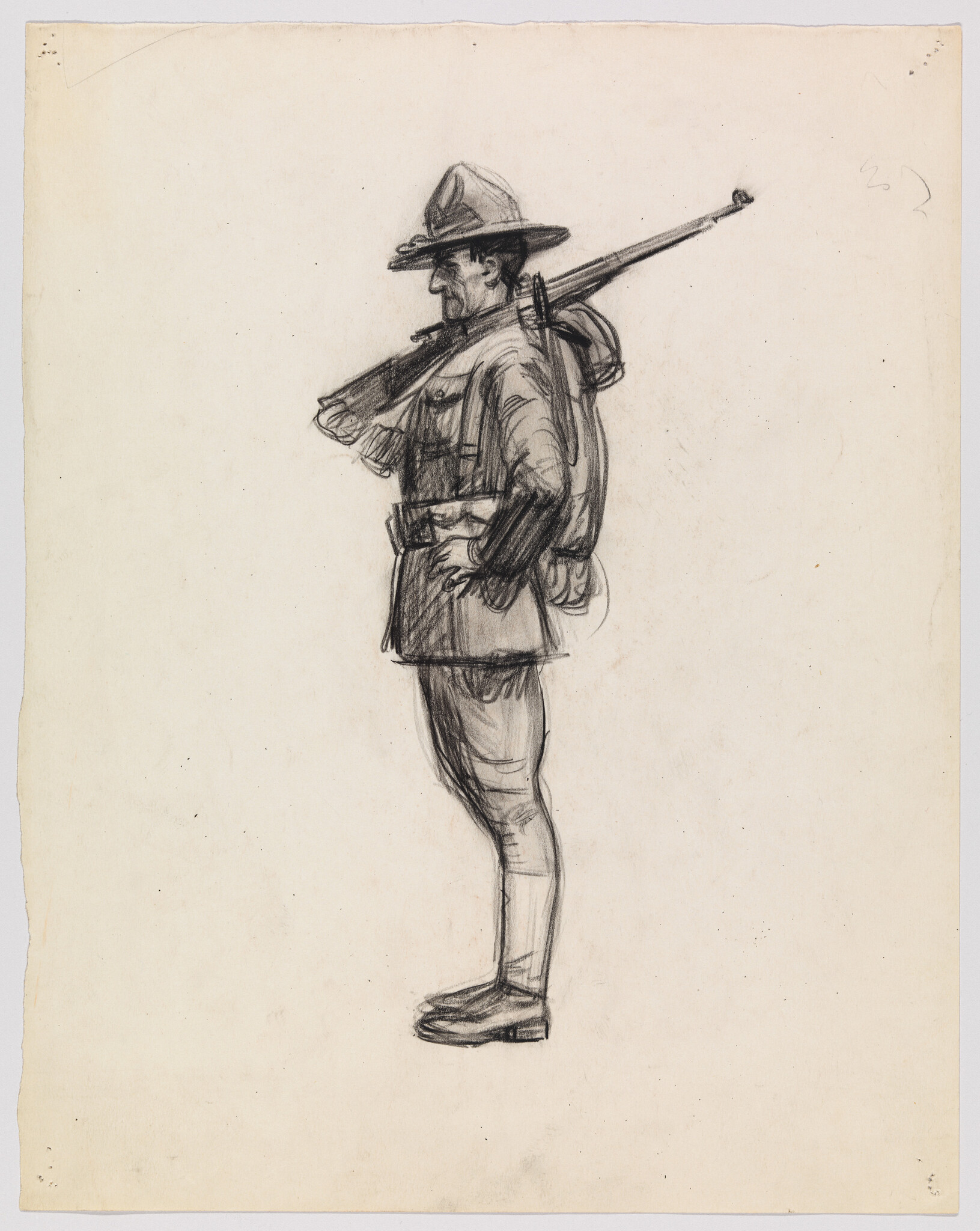 A standing soldier in uniform with a rifle slung over his shoulder and hands on hips.