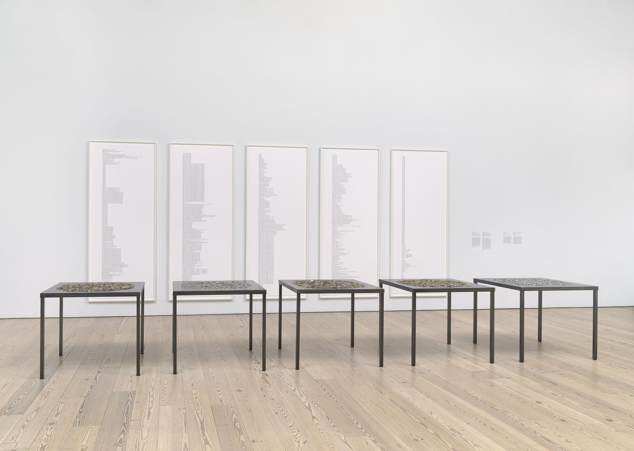 Five black tables with patterned surfaces stand in a row, with large framed charts or lists behind them.