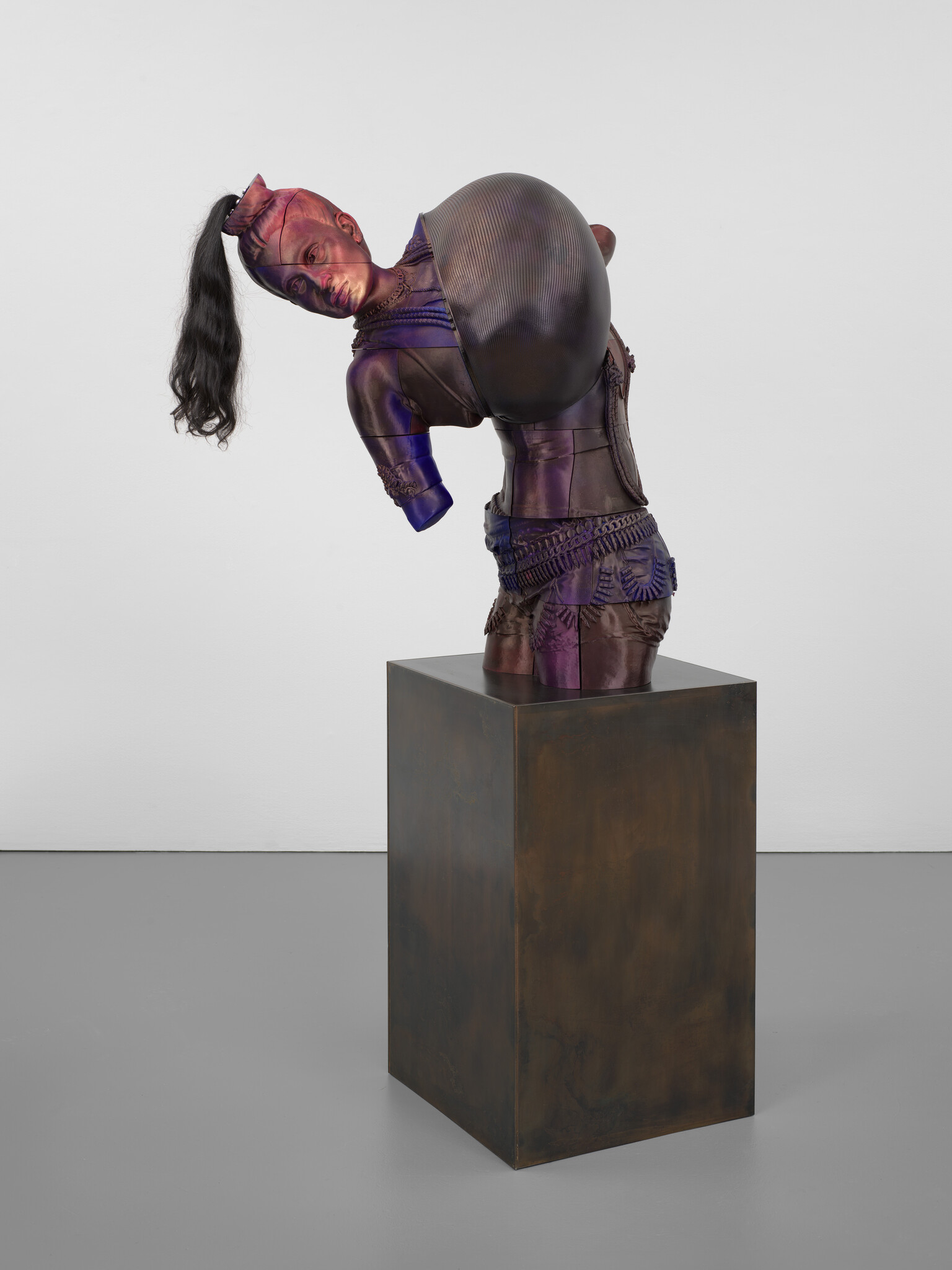 Sculpture of a headless figure with a ponytail, wearing armor, displayed on a pedestal.