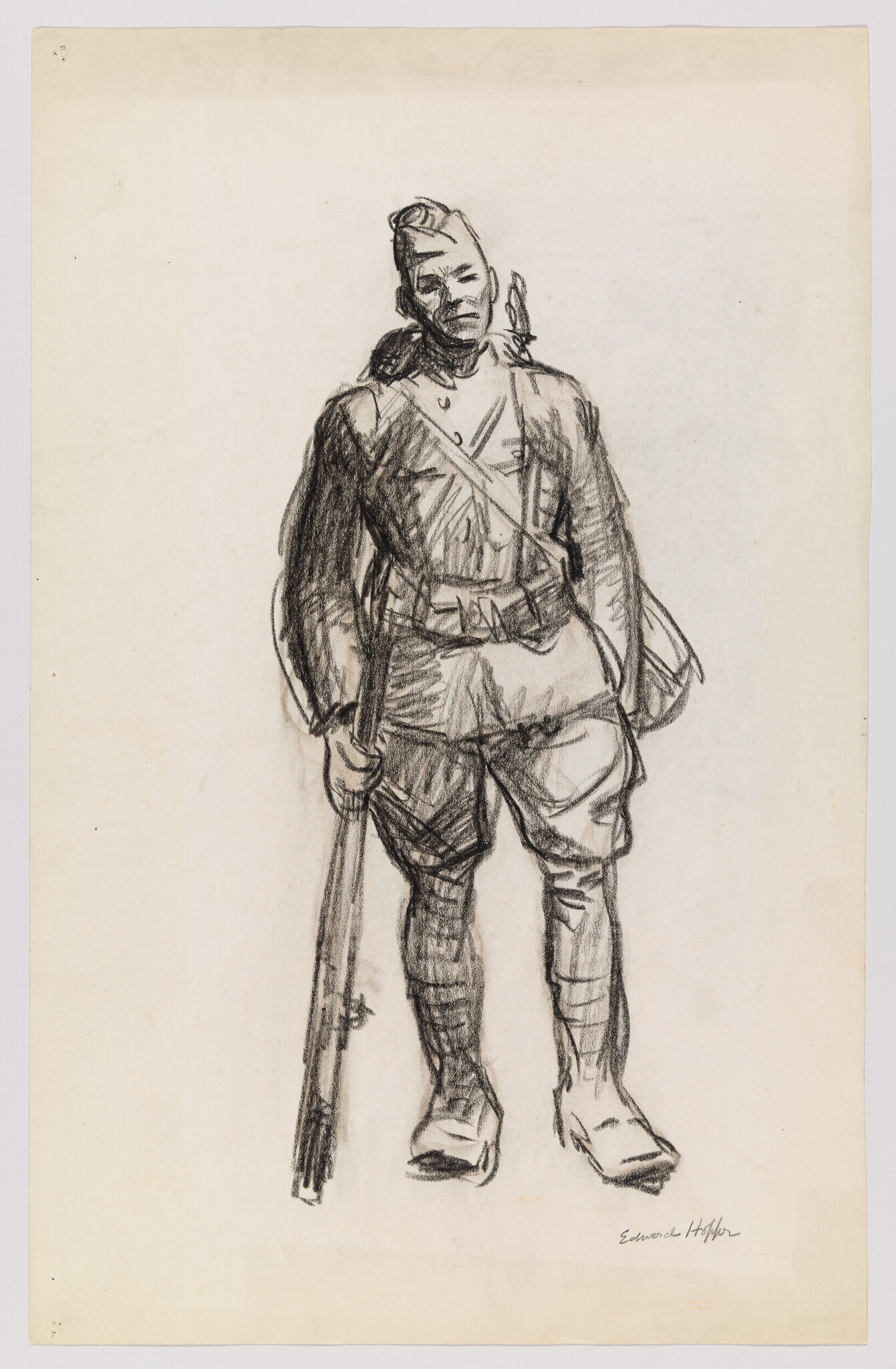 A soldier in uniform stands facing forward holding a rifle at his side.