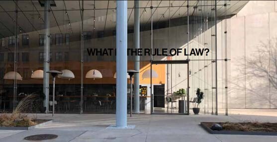 Large glass building entrance with the words “WHAT IS THE RULE OF LAW?” displayed in bold black letters.
