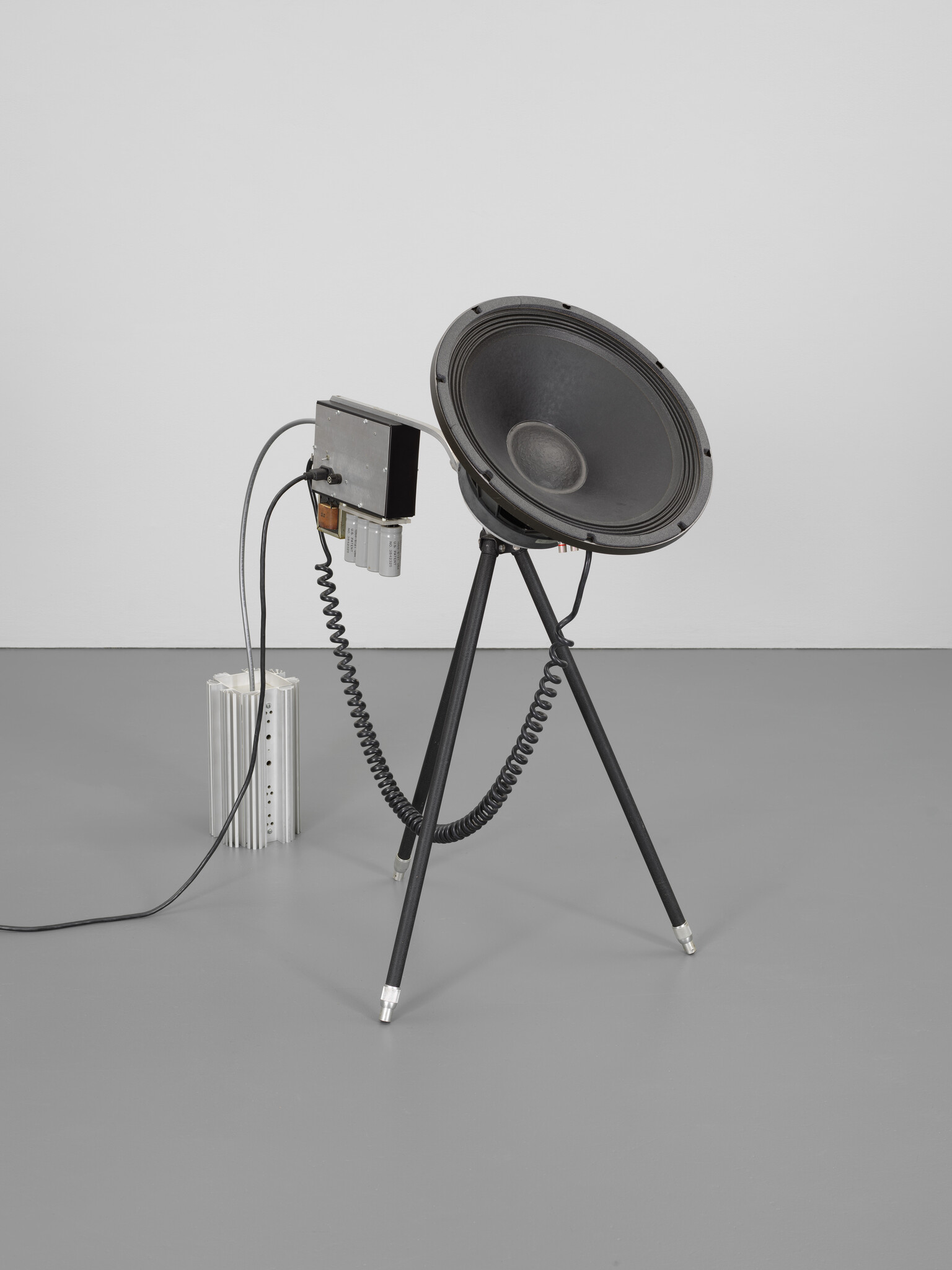 Large black loudspeaker cone mounted on a tripod with attached electronic box and coiled cables.