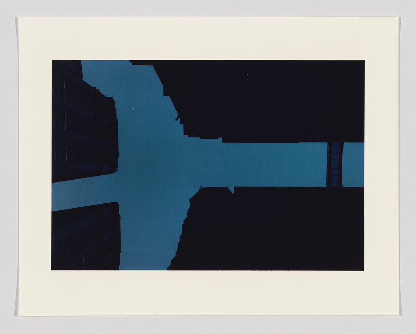 Tall buildings frame a cross-shaped patch of blue sky seen from street level.