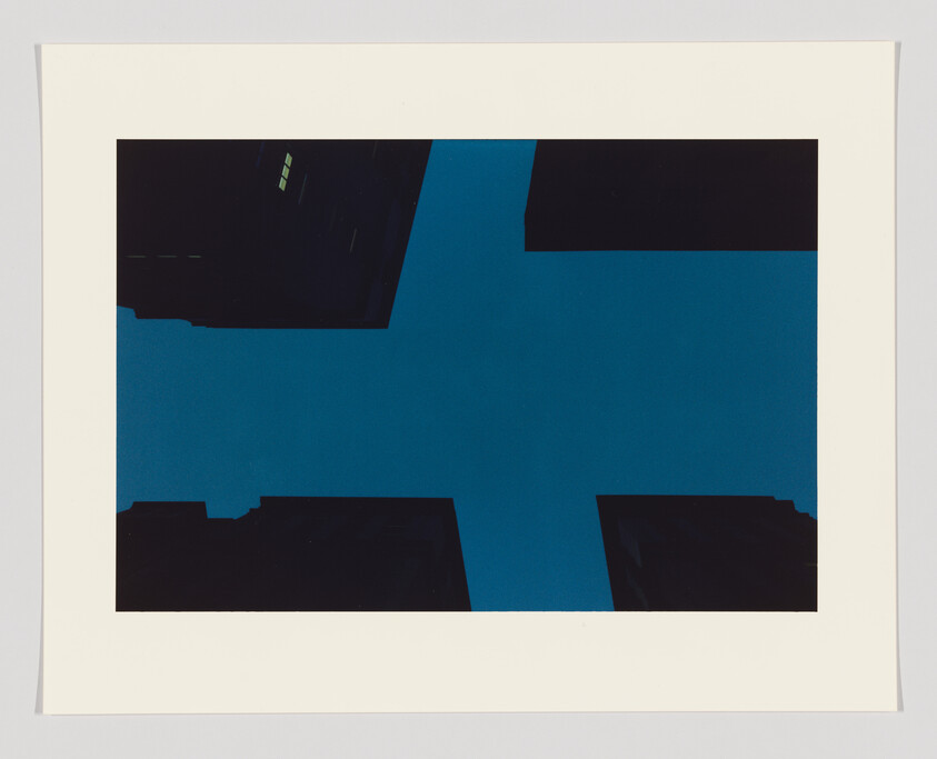 Tall dark buildings form a cross shape against a blue sky, with a few lit windows visible.