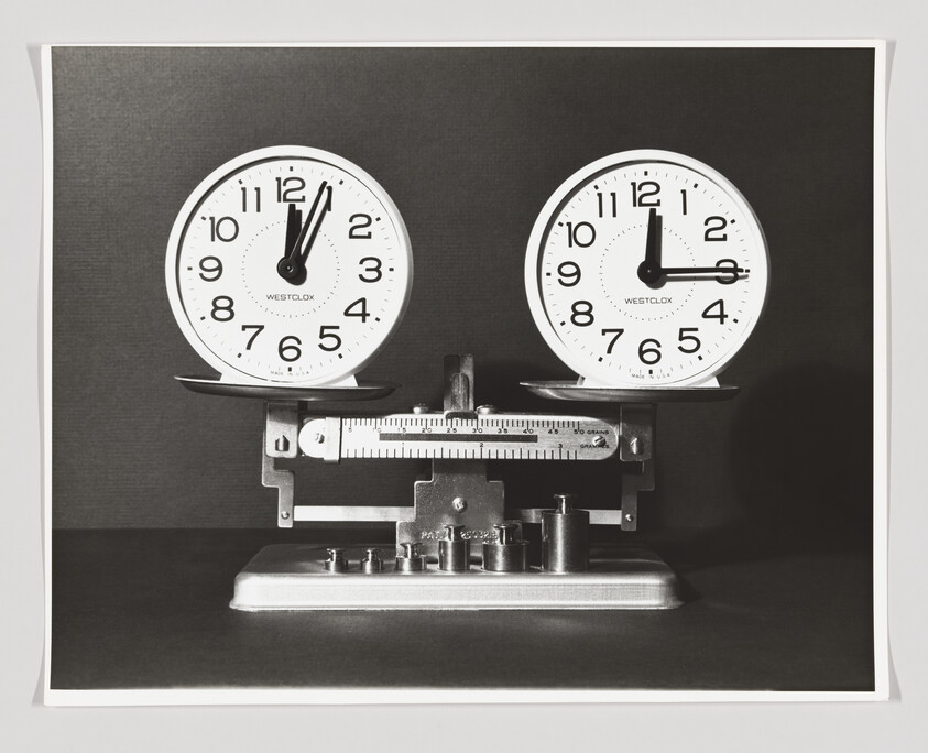A balance scale holding two round clocks showing different times.