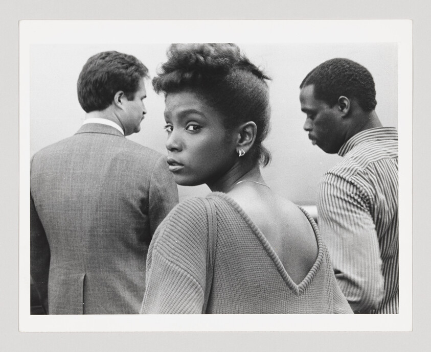 Woman glancing over shoulder with two men in conversation behind her, all in grayscale.