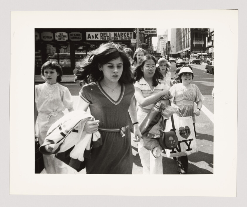 A group of girls hurriedly crosses a busy city street carrying bags, one with "I ♥ NY."