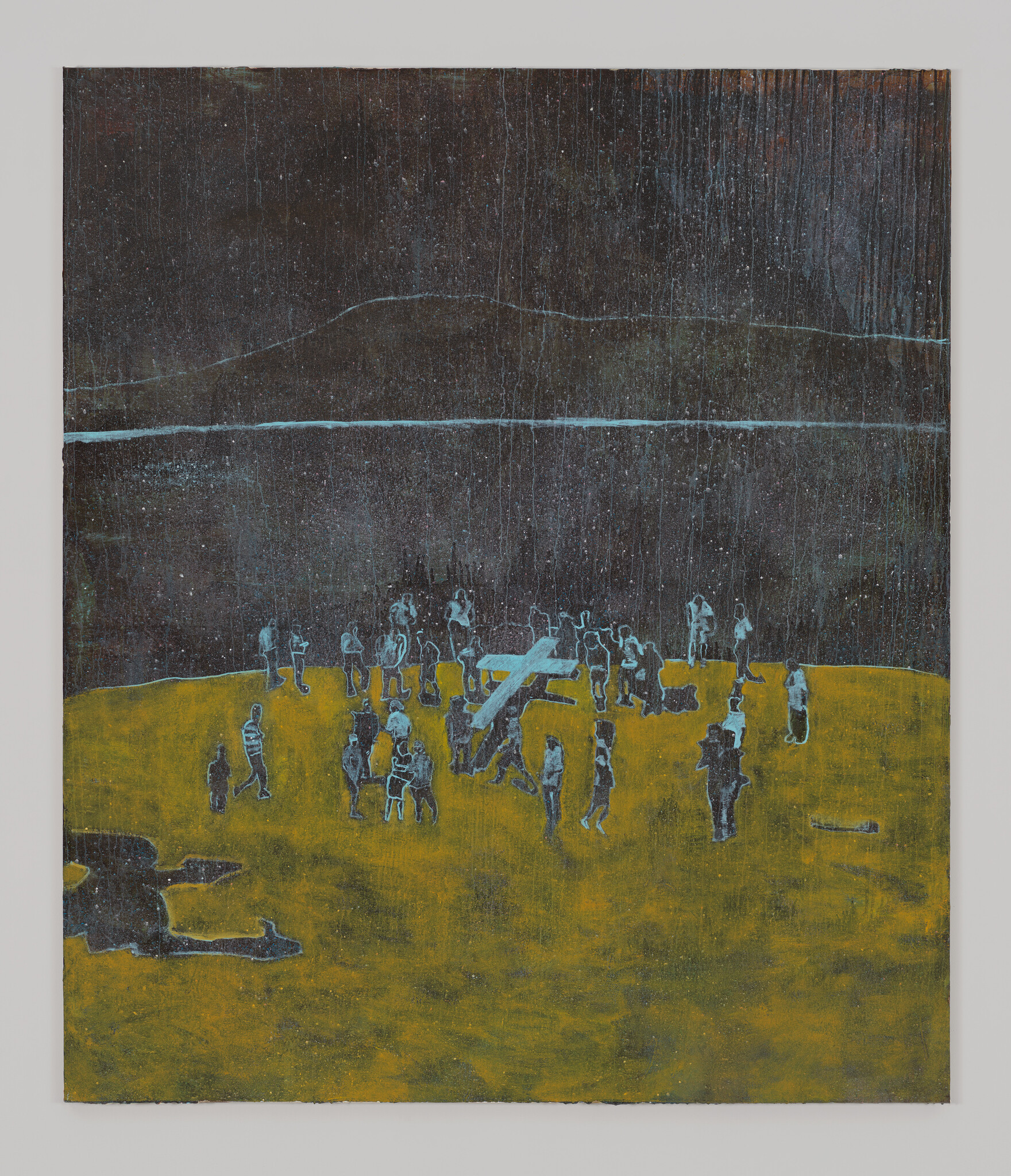 A group of people stand on a yellow field around others carrying a large wooden cross.