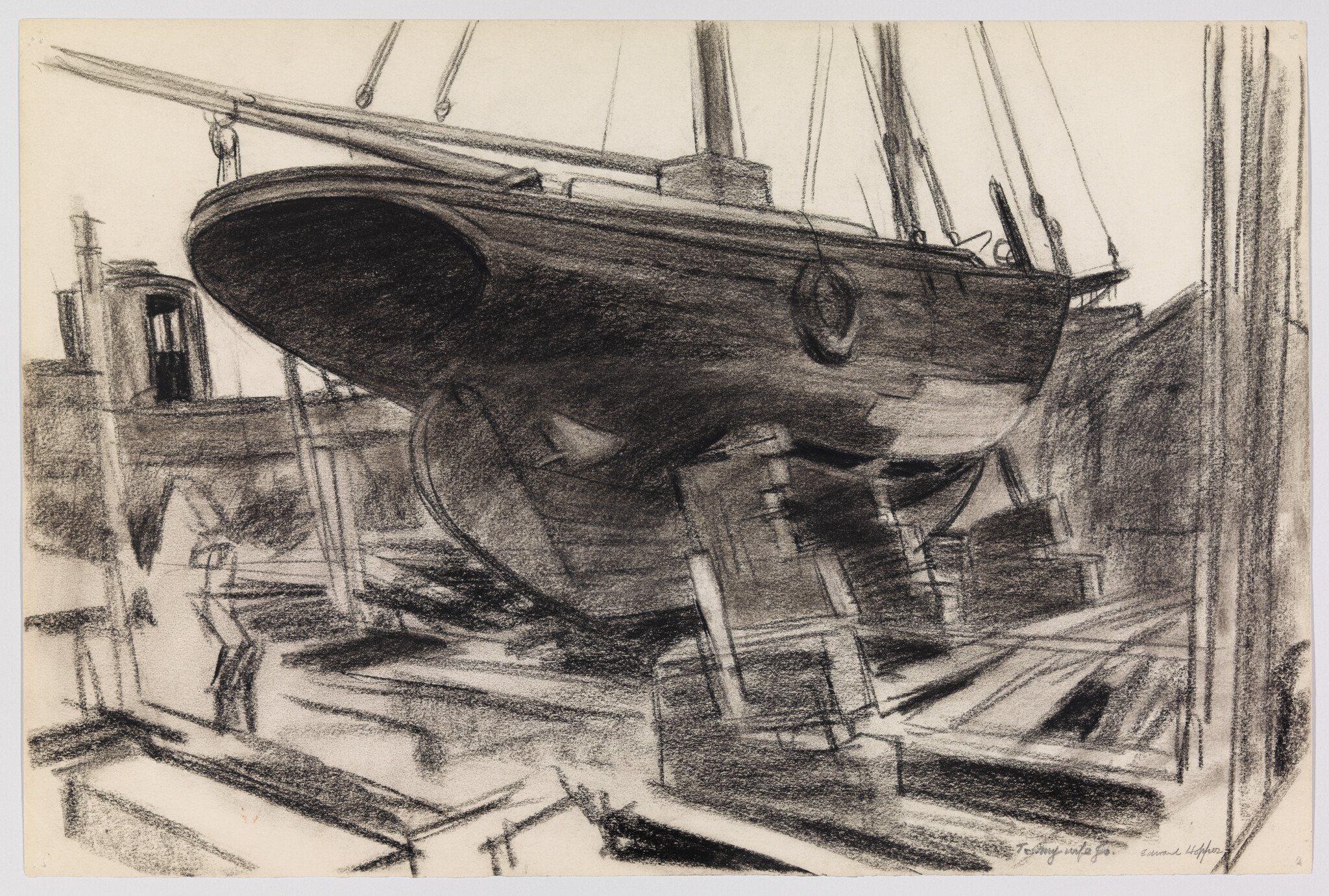 A large wooden sailboat hull sits on blocks in a shipyard dry dock.