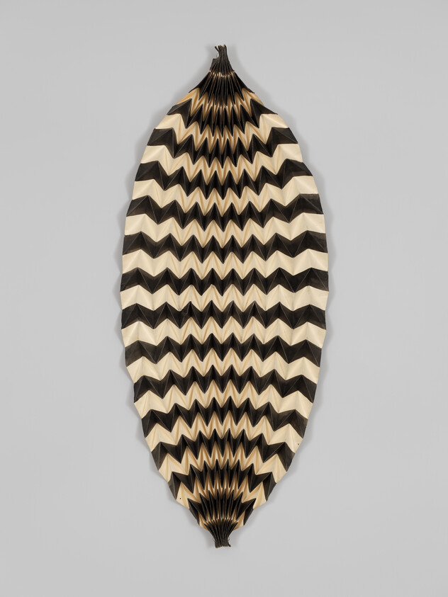 Long oval black-and-white chevron paper fan with accordion folds hanging against a gray background.