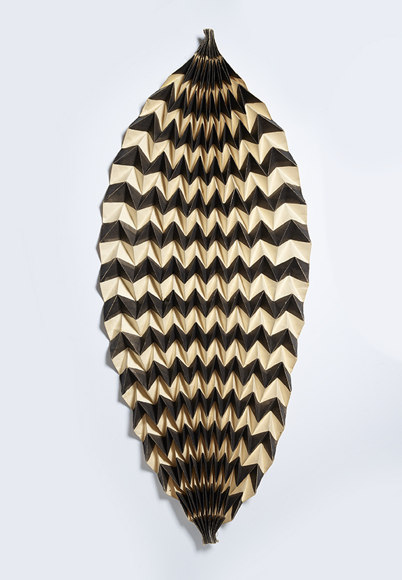 Geometric, leaf-shaped paper sculpture with a zigzag pattern in black and beige, creating a textured, three-dimensional effect.