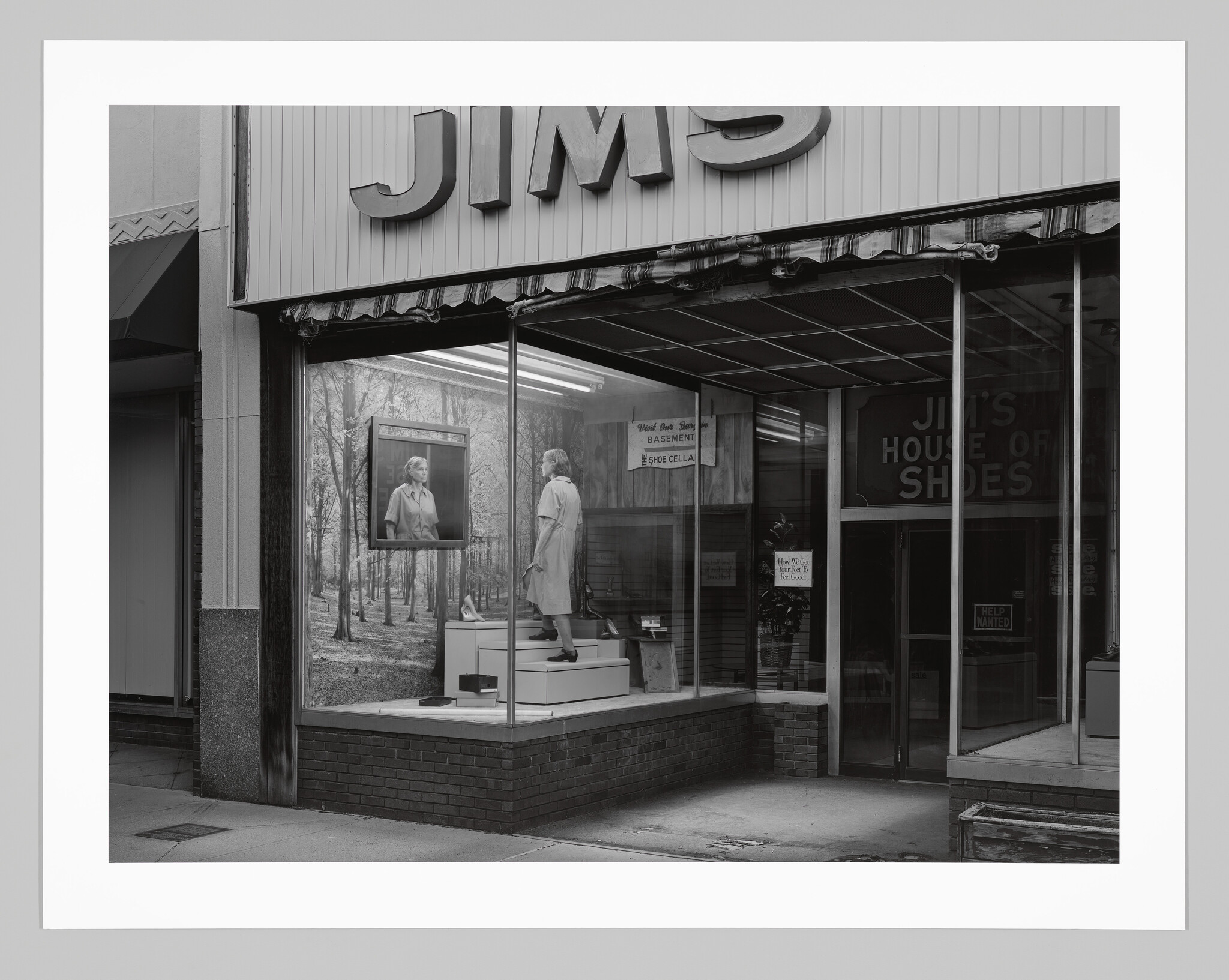 Storefront window display with a female mannequin, shoe boxes, and signs reading “Used Shoe Sale” and “Help Wanted.”