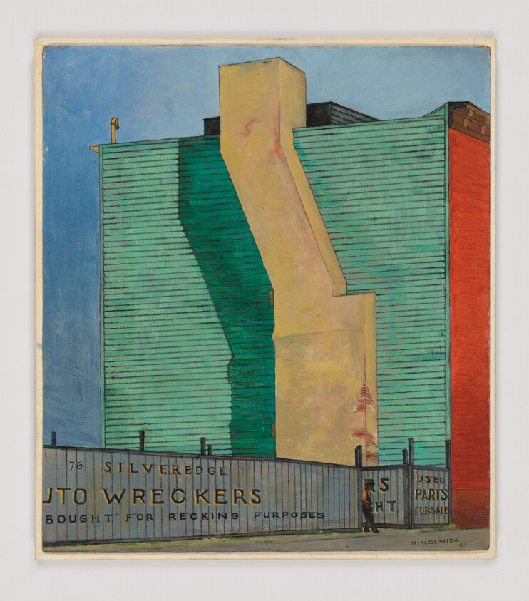 Large teal industrial building with a yellow exhaust chute behind a fence reading Auto Wreckers, a person walking nearby.