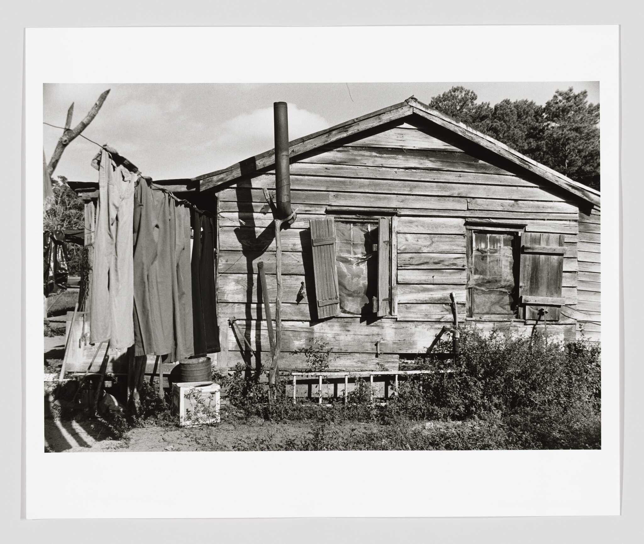Weathered wooden shack with open shutters and clothes hanging on a line beside it.
