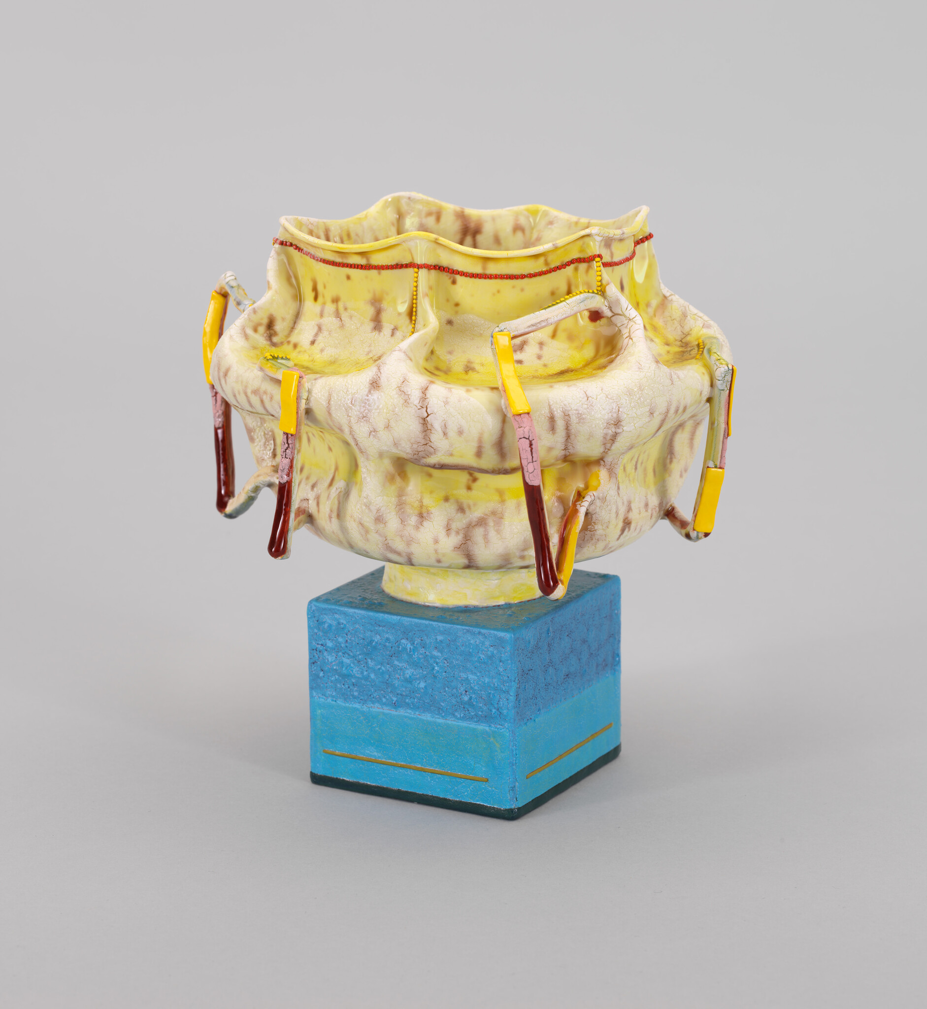 A yellow, textured ceramic bowl with red and yellow accents sits atop a blue, rectangular base.
