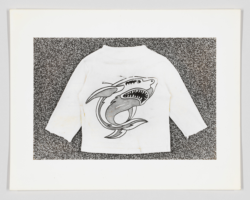 White long-sleeved shirt with a shark graphic, displayed on a speckled background.