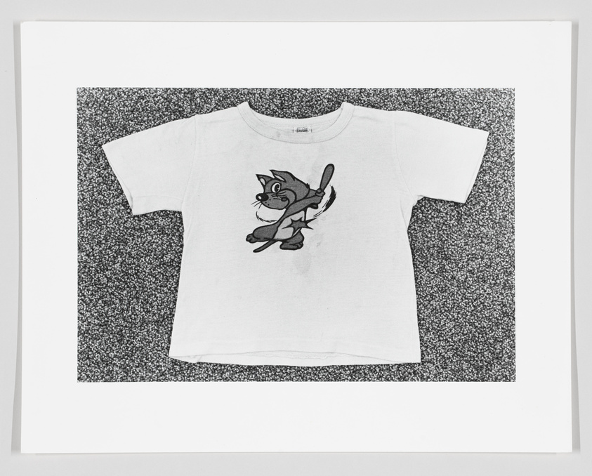 White t-shirt with a cartoon cat print, displayed on a speckled background.