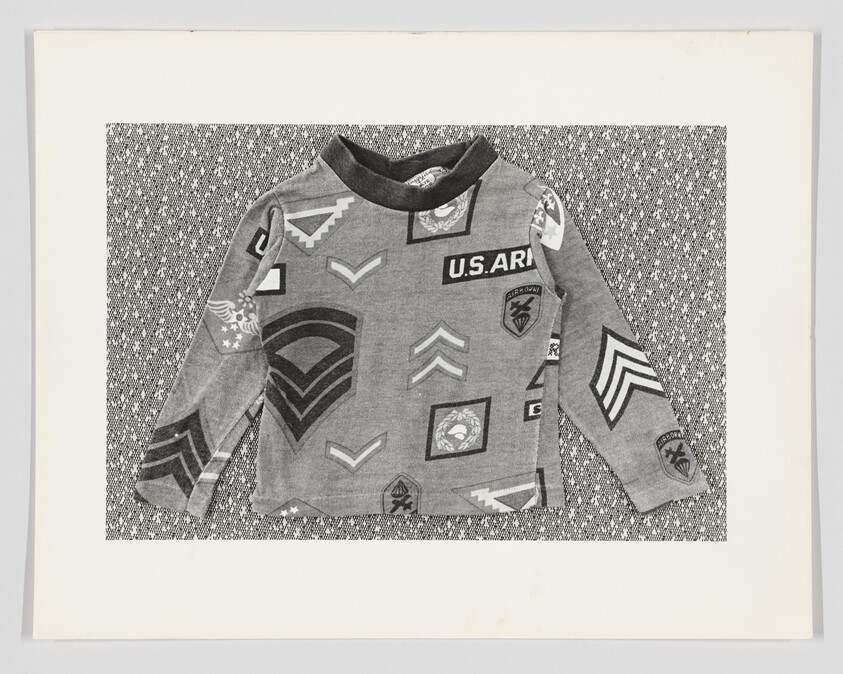 A child's grey camouflage shirt with various military-style patches on a patterned background.