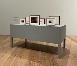 A display table with several framed photographs arranged on top in an art gallery setting.