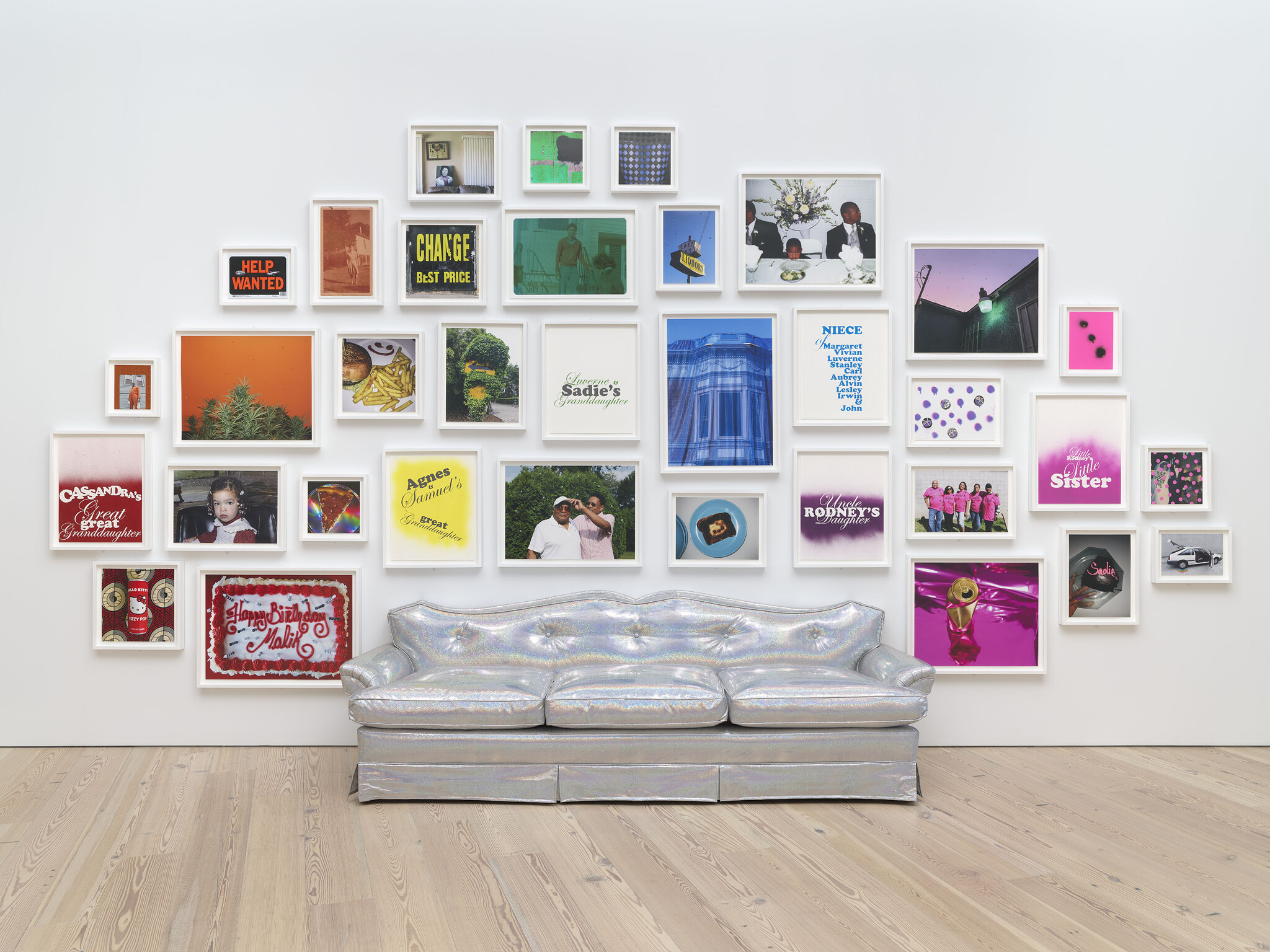 A shiny silver couch sits in front of a wall covered with colorful framed photos, signs, and family names.