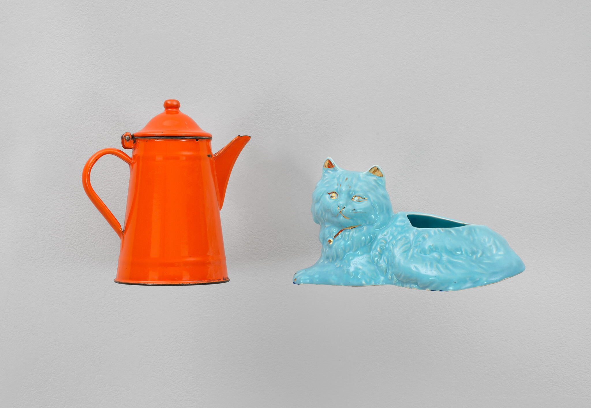 An orange teapot and a blue cat-shaped teacup on a white background.