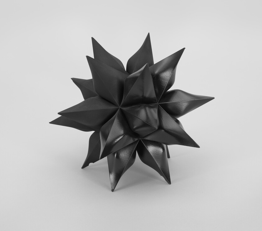 A black glossy geometric star sculpture with multiple sharp points resting on a white surface.
