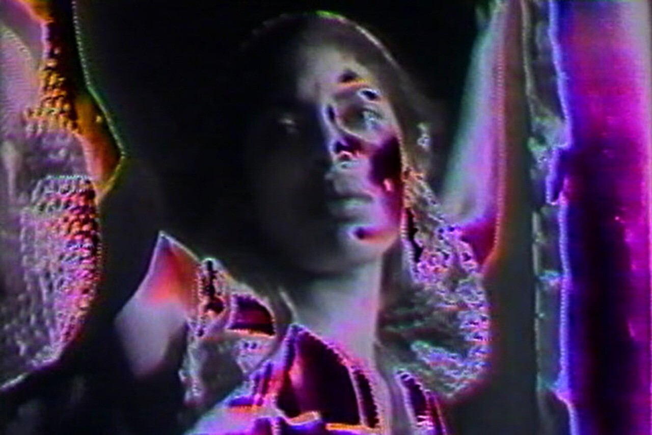 Young woman with neon distorted colors raises her arms against a dark background.