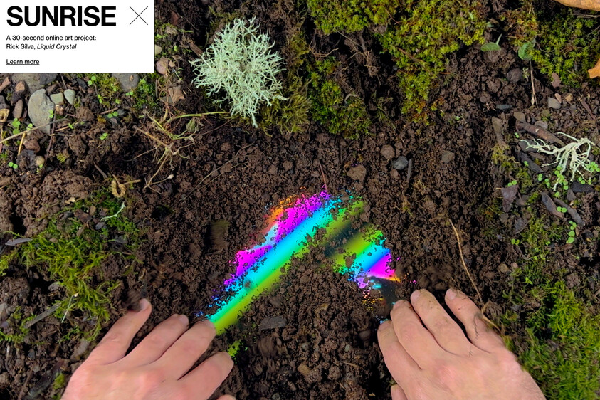 Two hands part soil to reveal a bright rainbow-colored iridescent streak in dirt.