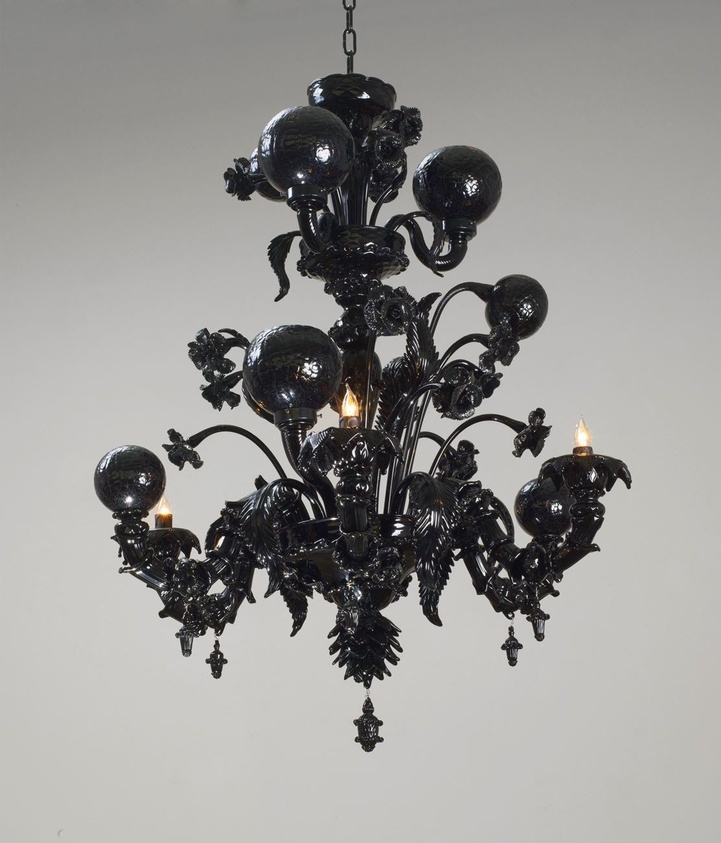 Ornate black chandelier with intricate floral designs and glowing bulbs, hanging against a plain background.