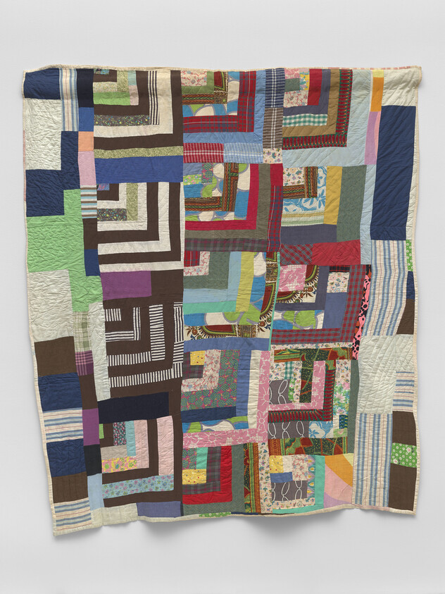 Colorful patchwork quilt made of various patterned fabric strips arranged in log cabin-style square blocks.
