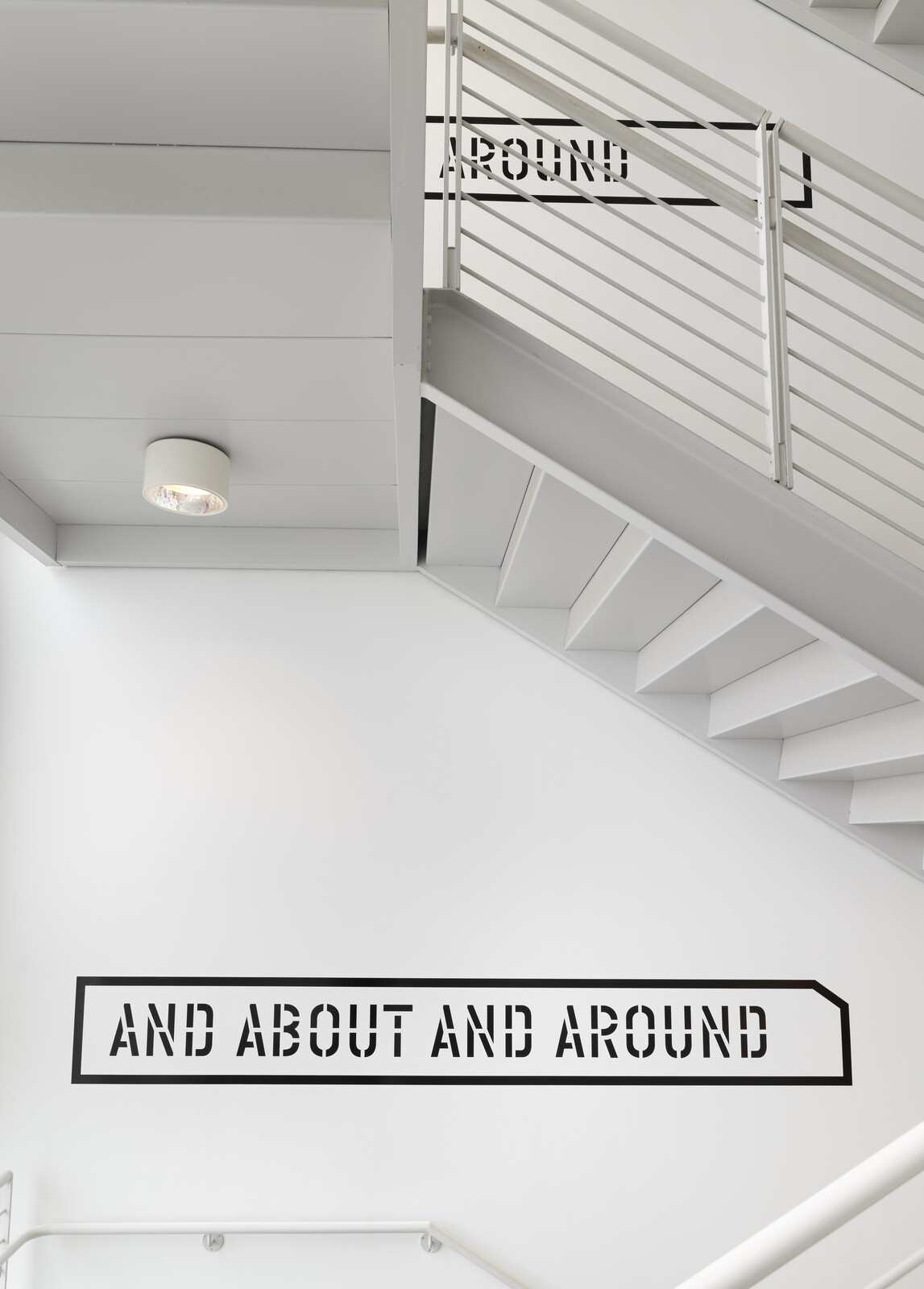 White stairwell with metal railing and wall text reading "AND ABOUT AND AROUND."