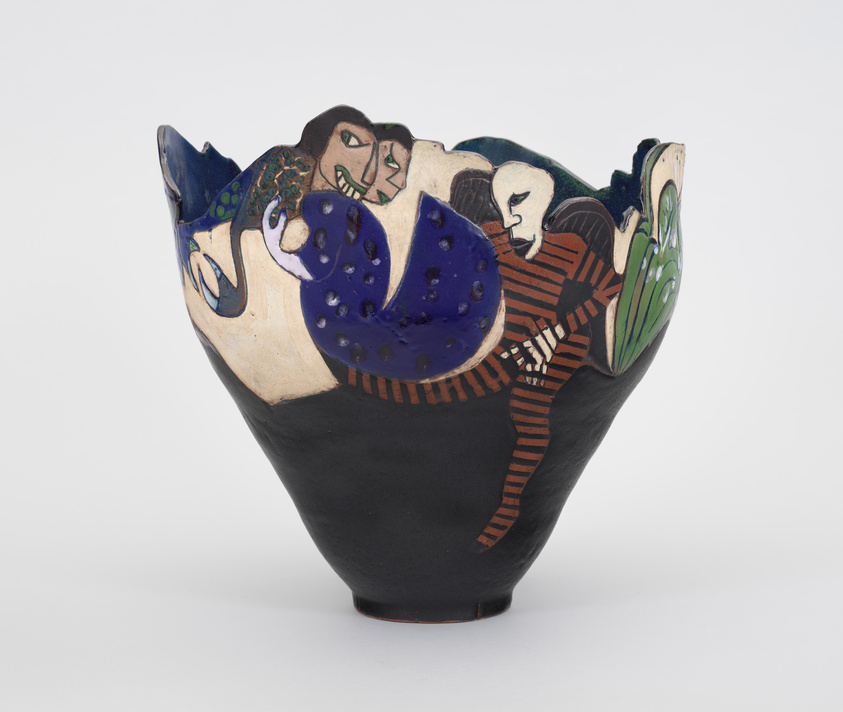 Decorative ceramic vase with colorful, abstract figures including a blue creature, a striped figure, and a green element on a black base.