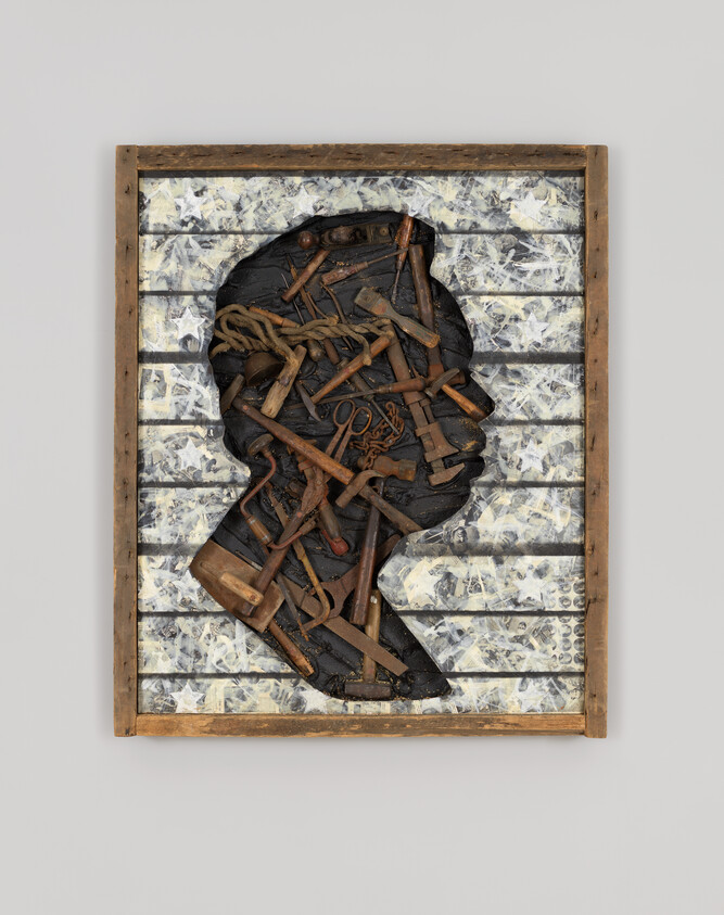 A wooden frame holds a side profile silhouette filled with old tools, rope, and metal objects against a patterned background.