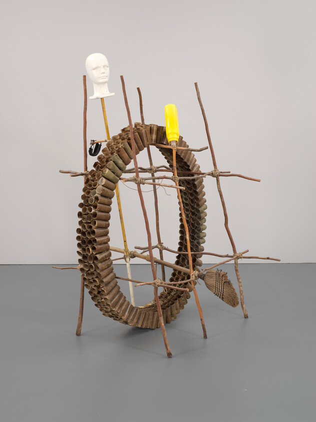 Sculpture with a circular wooden structure, yellow mask, and white mannequin head on top.