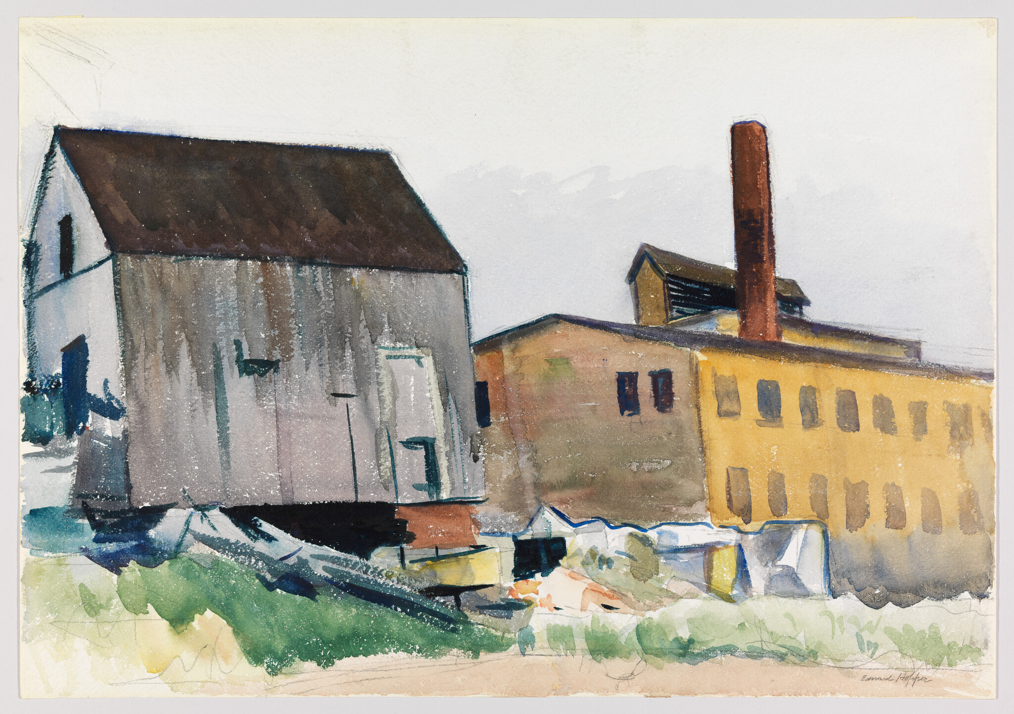 Two industrial buildings and a tall brick smokestack beside a grassy foreground.