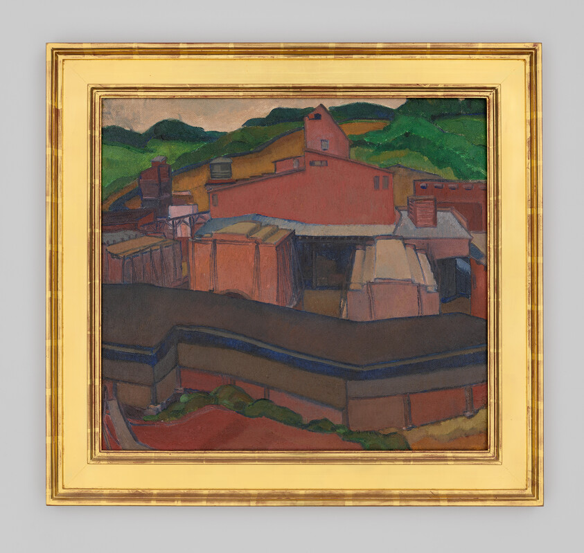 Several red and brown industrial buildings with angular roofs sit in front of green hills under a light sky.