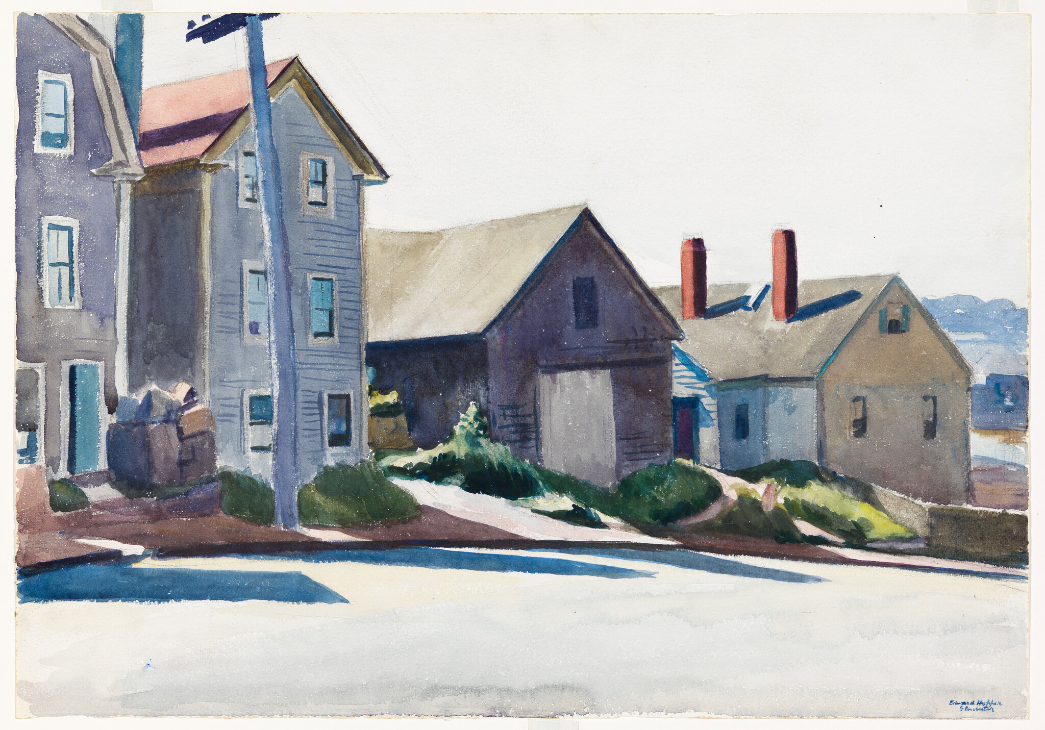 A row of clapboard houses and sheds cast long shadows along a sunlit coastal street.