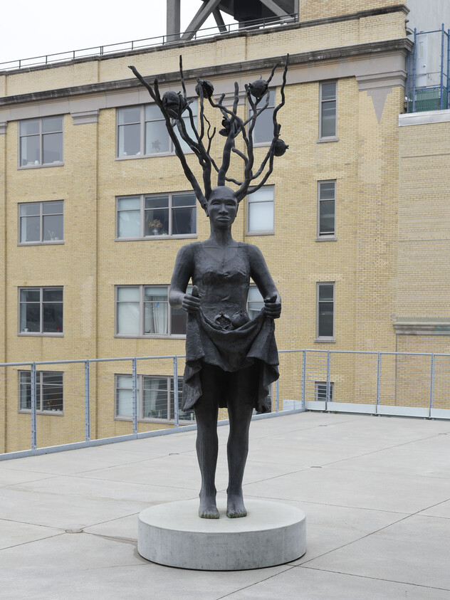 Bronze statue of a standing woman holding up her skirt with tree-like branches growing from her head.