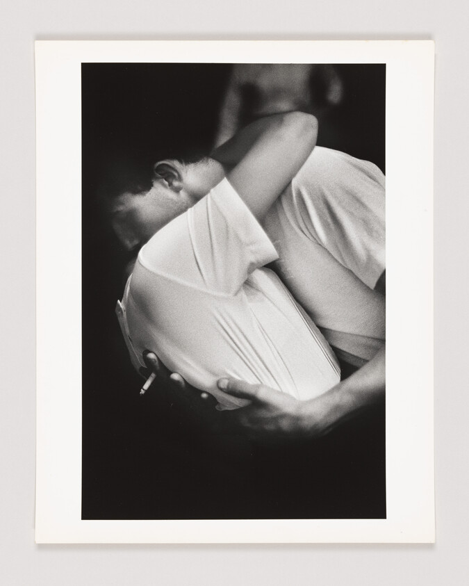 Two people embrace tightly while one person holds a cigarette behind the other's back.