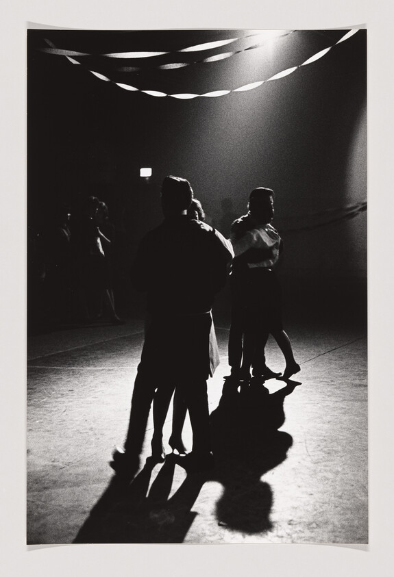 Couples slow dancing under streamers in a dim hall, their long shadows stretching on the floor.