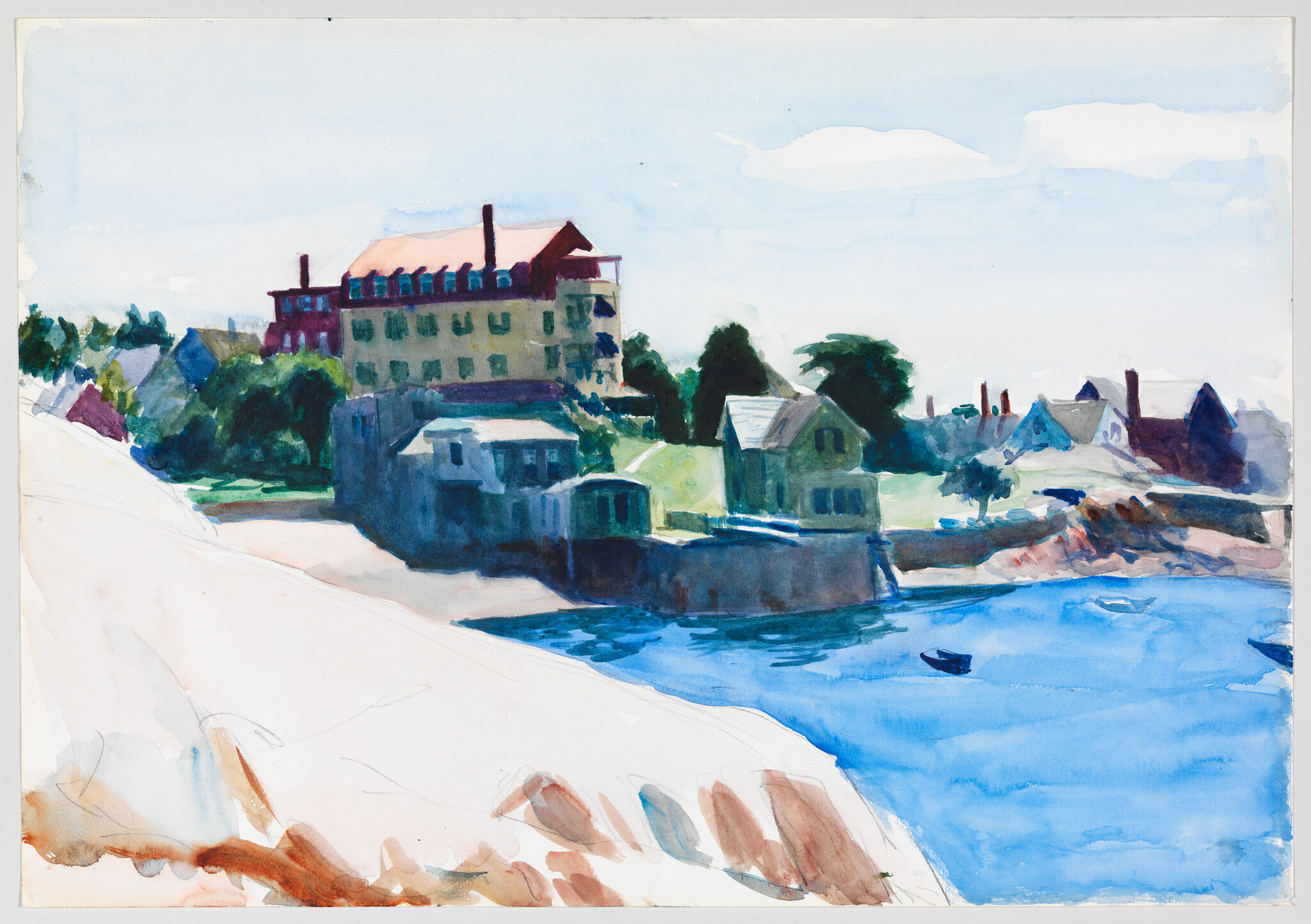 A row of waterfront houses and a large hotel beside calm blue water with small boats.