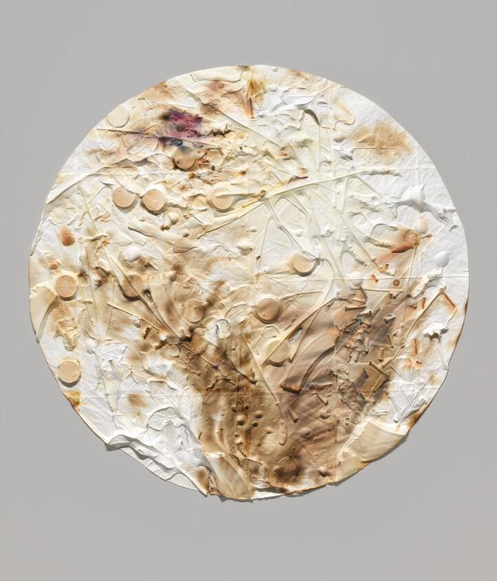 A circular textured artwork with cream and brown smudges, raised shapes, on a gray background.