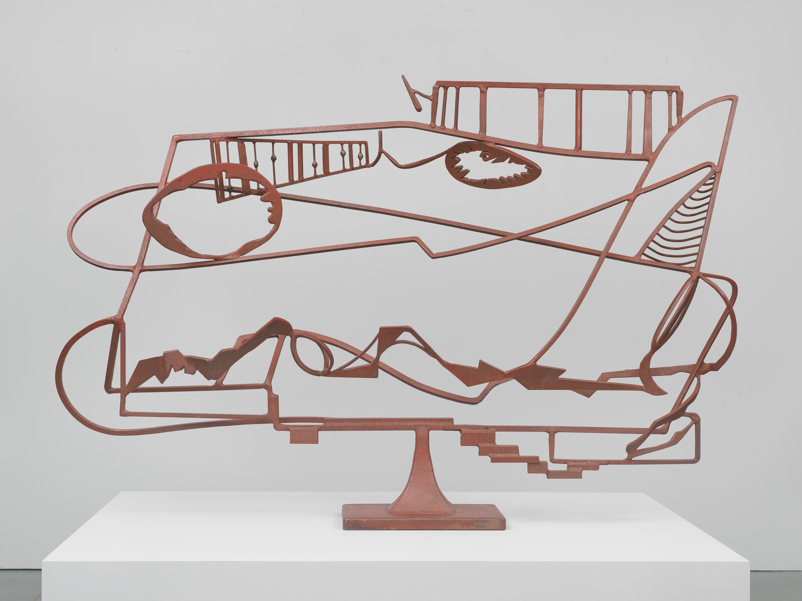 Abstract metal sculpture with geometric shapes and lines on a white pedestal.