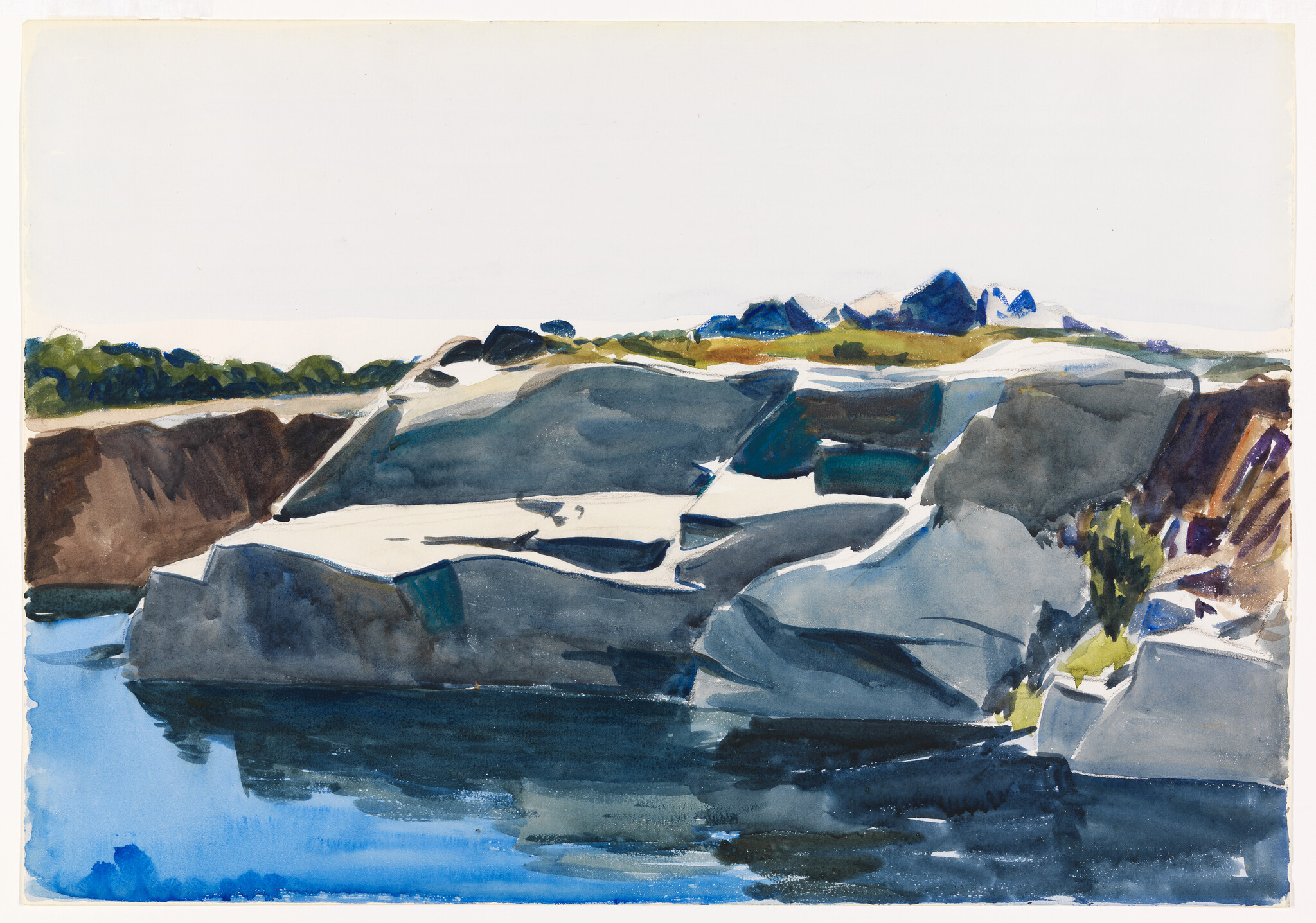 Large gray rocks along calm blue water with reflections and distant tree-lined shore.