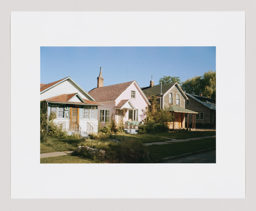Three small suburban houses with front porches and lawns under a clear blue sky.
