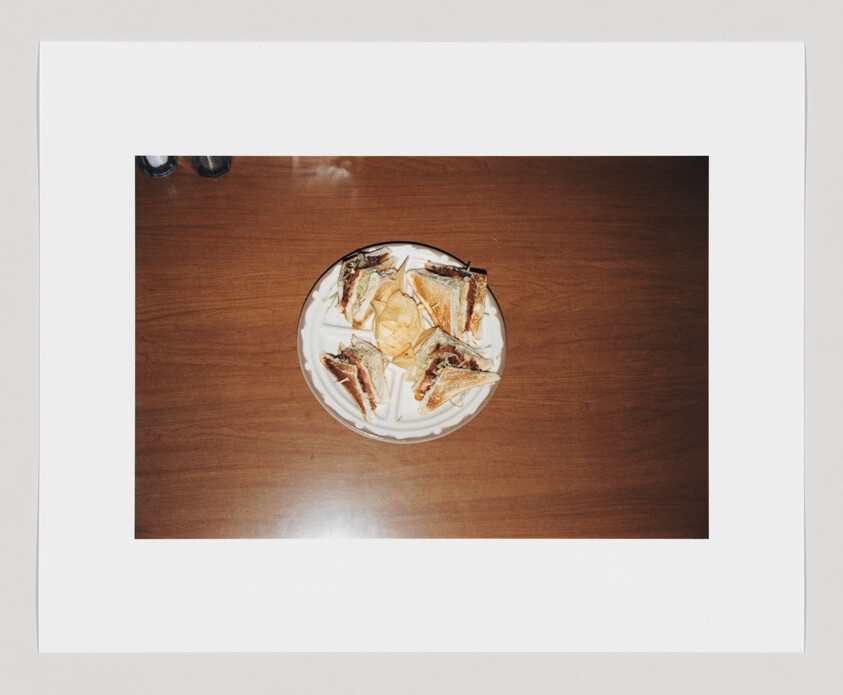 A plate of triangular sandwich halves arranged around potato chips on a wooden table.