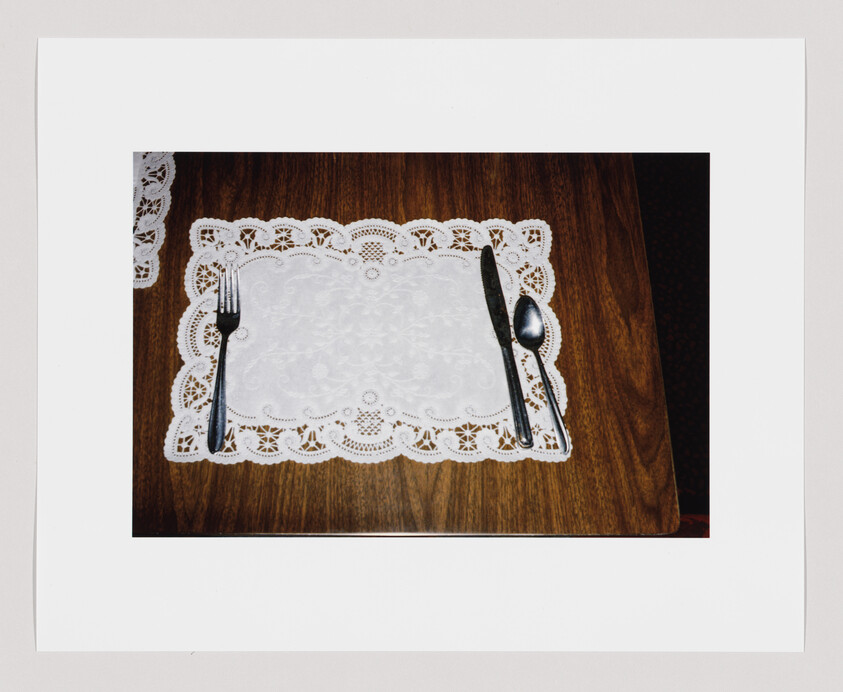 A fork, knife, and spoon are placed on a lace placemat on a wooden table.