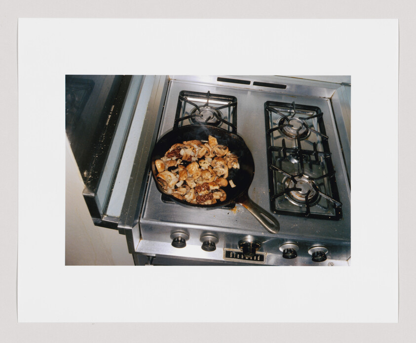 A frying pan with cooked mushrooms and onions sits on a gas stove with two burners.